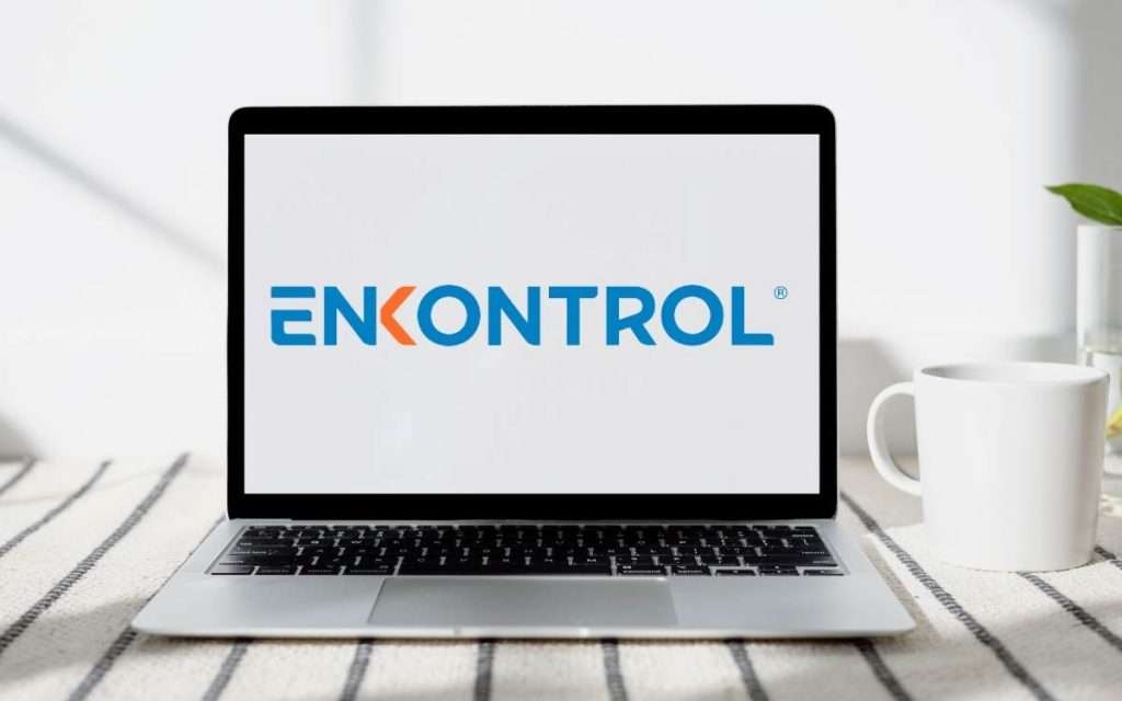 En la imagen se ve el logo de software enkontrol en la pantalla de una lapton sobre una mesa de madera blanca.